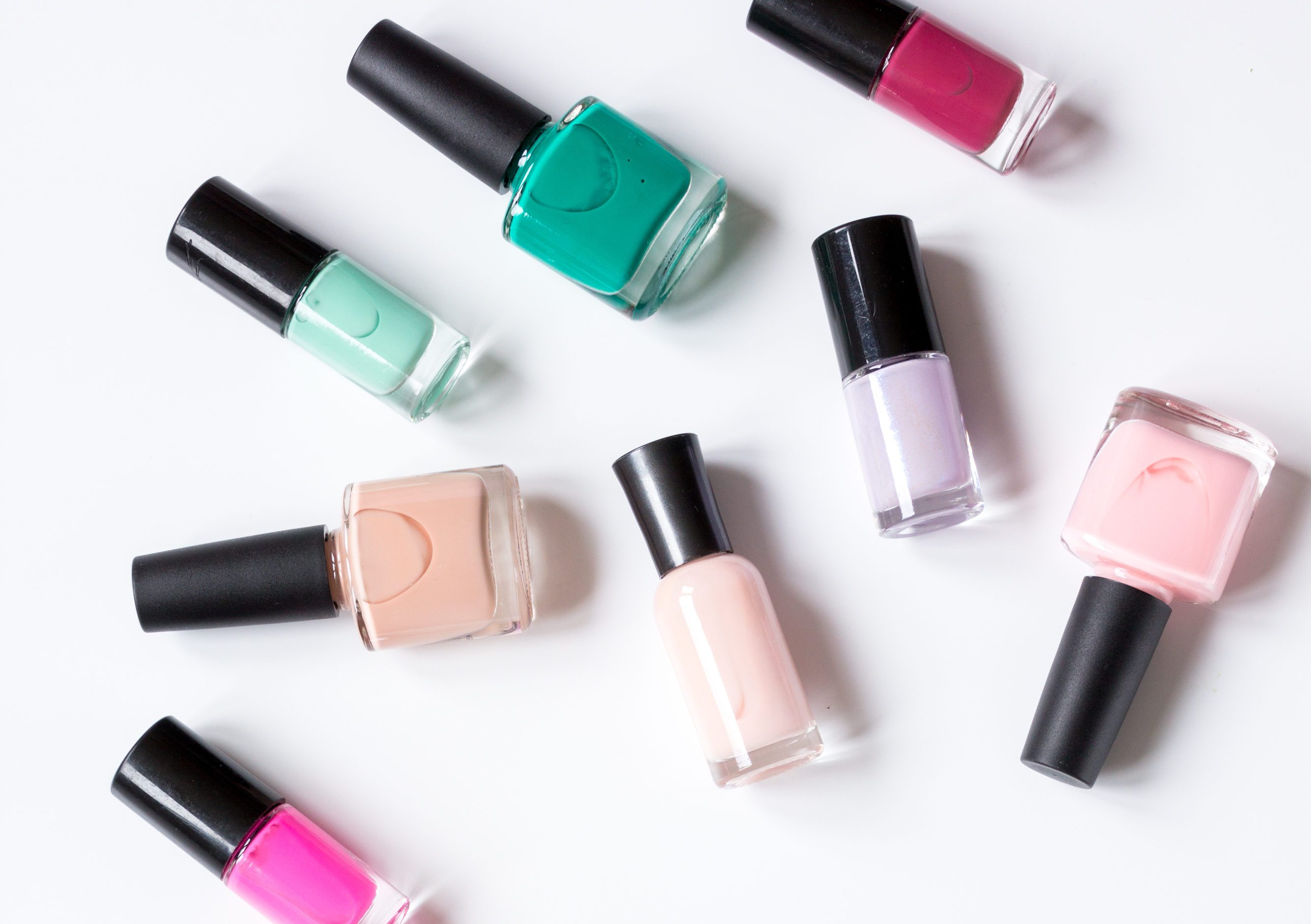 Nail polish bottles arranged randomly on a white surface display a variety of colors, including pink, green, and purple.