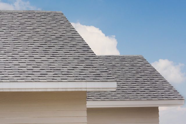 Gray shingled roof sits beneath a blue sky with scattered clouds. Light-colored siding is visible below the roof.