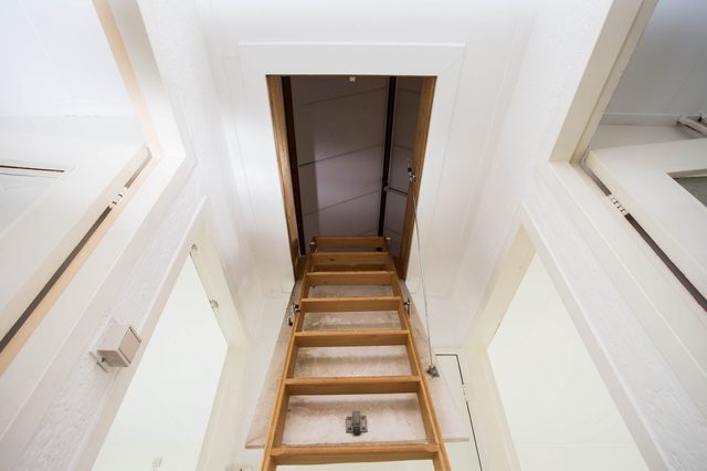 Wooden ladder extends upwards through an attic hatch in a white room with open doorways.