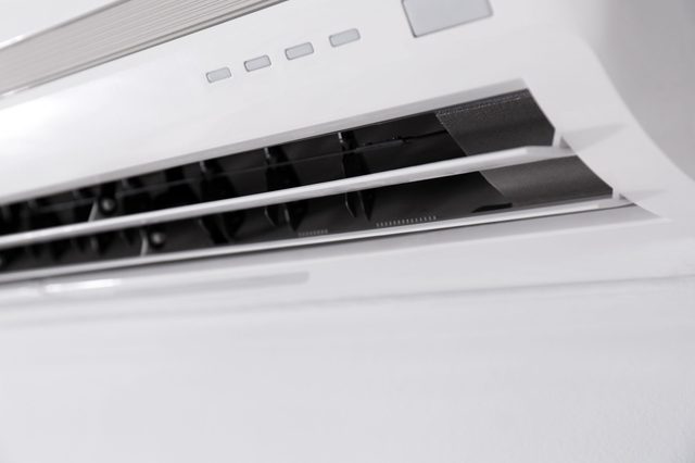 Air conditioning unit blows air, mounted indoors on a white wall.