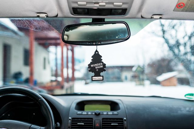 Air freshener hangs from the rearview mirror inside a car, with a snowy landscape visible through the windshield.