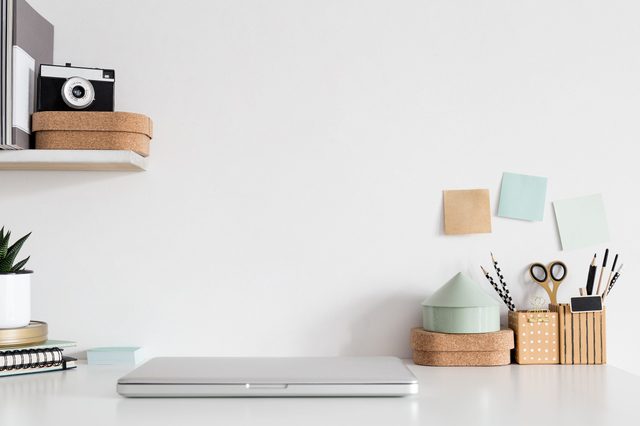 Laptop rests closed on a tidy desk surrounded by stationery, plants, and pastel sticky notes on a white wall.
