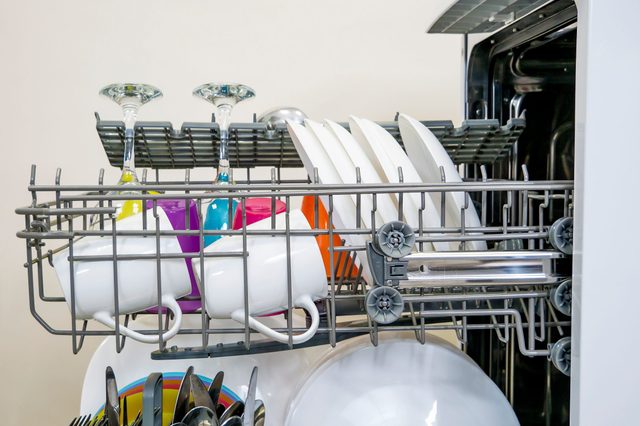 Dishwasher rack holding clean cups, glasses, and plates inside a modern kitchen appliance.