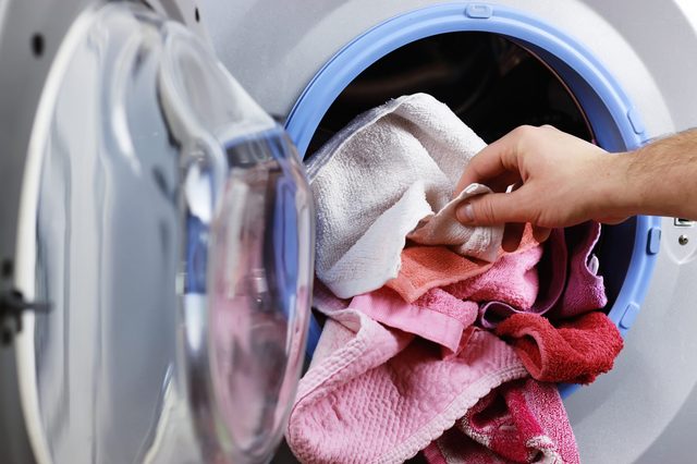 Hand places colorful towels into a front-loading washing machine, with a focus on its blue-rimmed door in a laundry room setting.