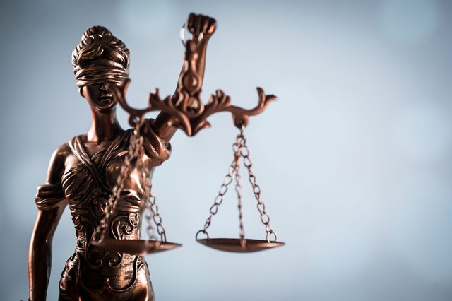 A bronze statue of Lady Justice holds balanced scales, set against a soft-focus background.