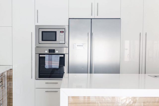 A modern kitchen features a microwave above an oven, a striped towel hangs, and a large stainless steel refrigerator nearby.