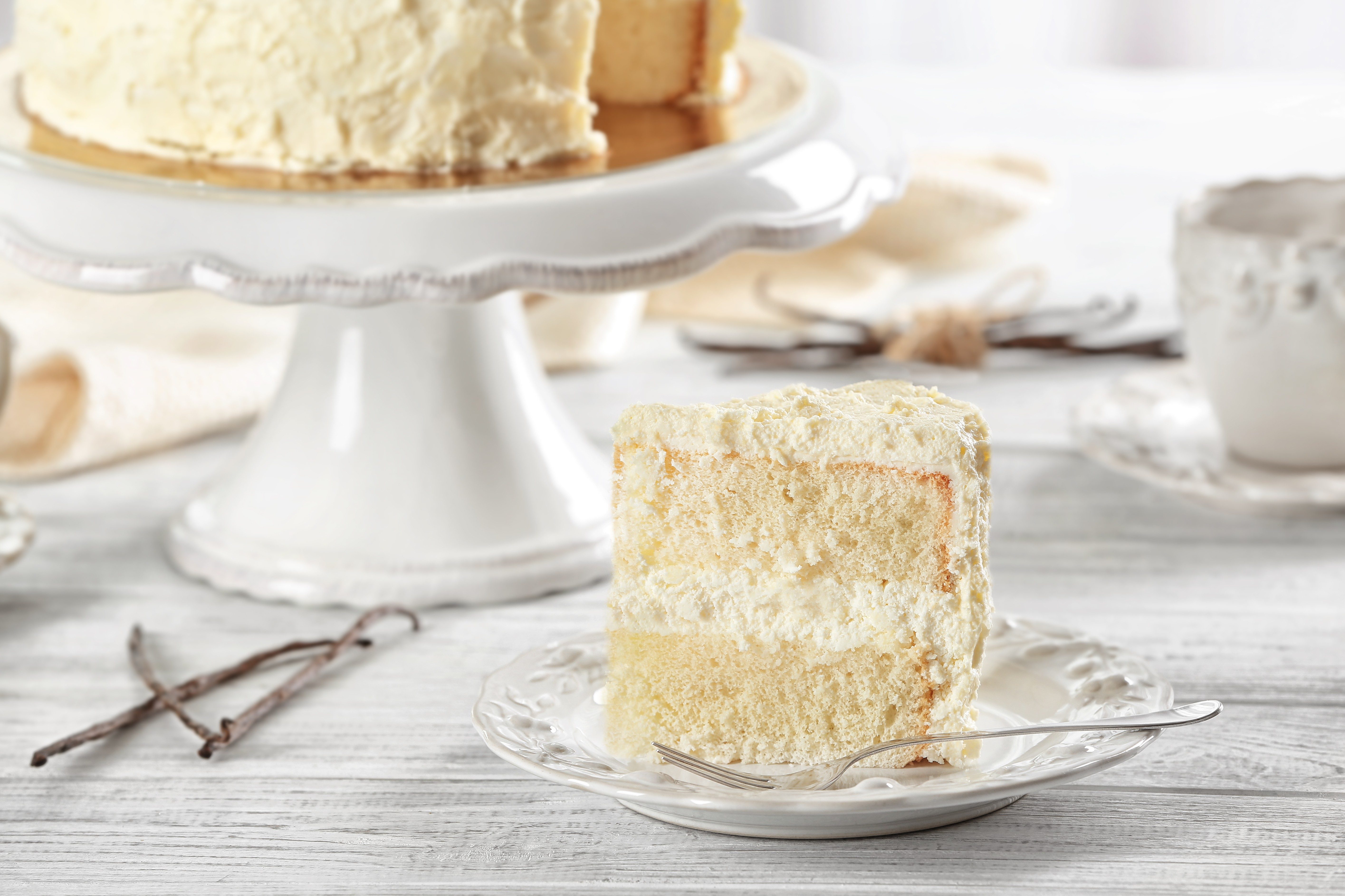 A slice of white cake rests on a decorative plate with a fork, surrounded by a bright, cozy kitchen setting.