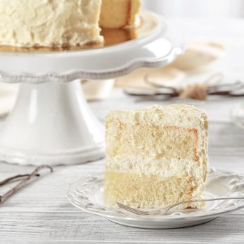 A slice of white cake rests on a decorative plate with a fork, surrounded by a bright, cozy kitchen setting.