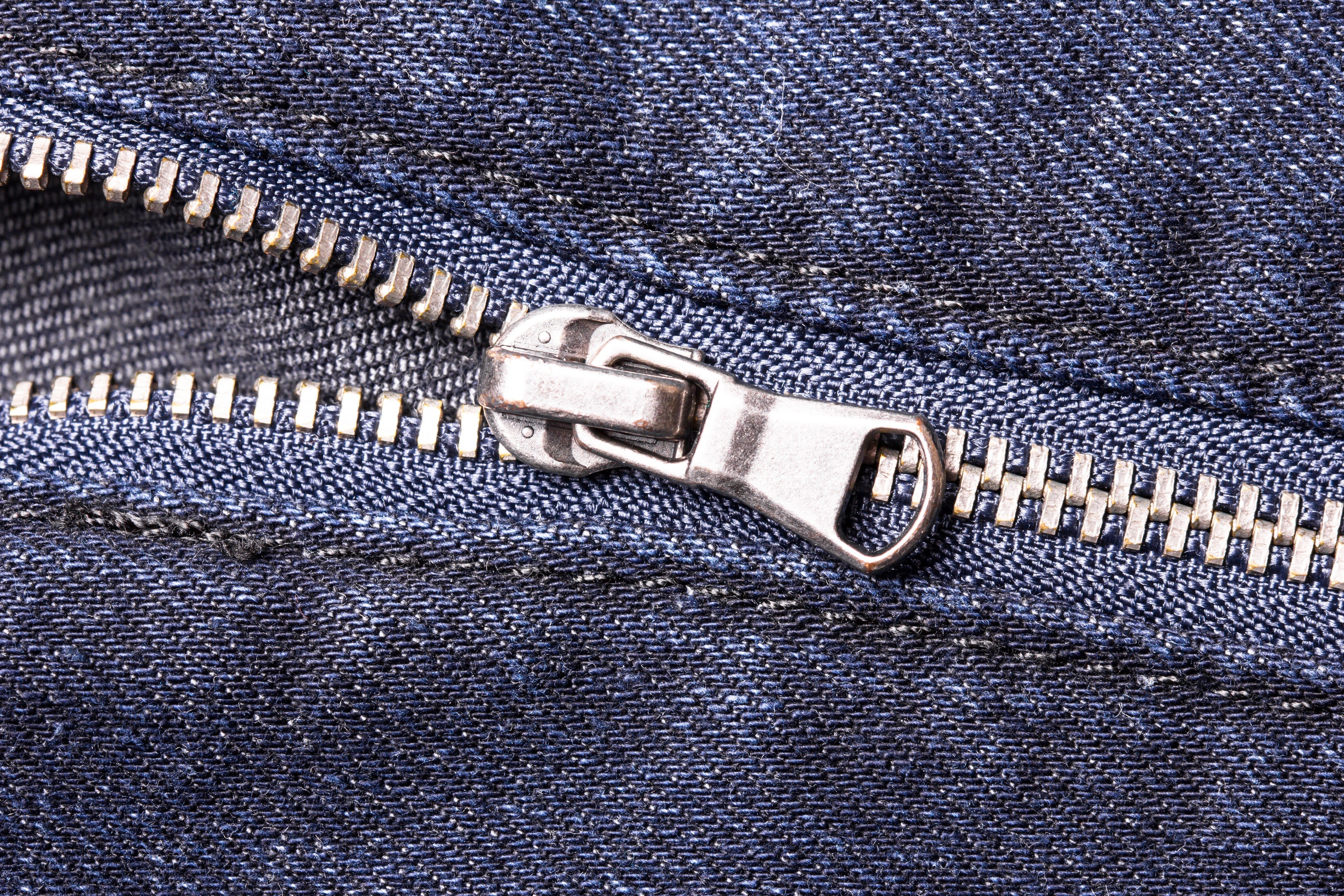 A metallic zipper is partially unzipped, set against a background of textured blue denim fabric.