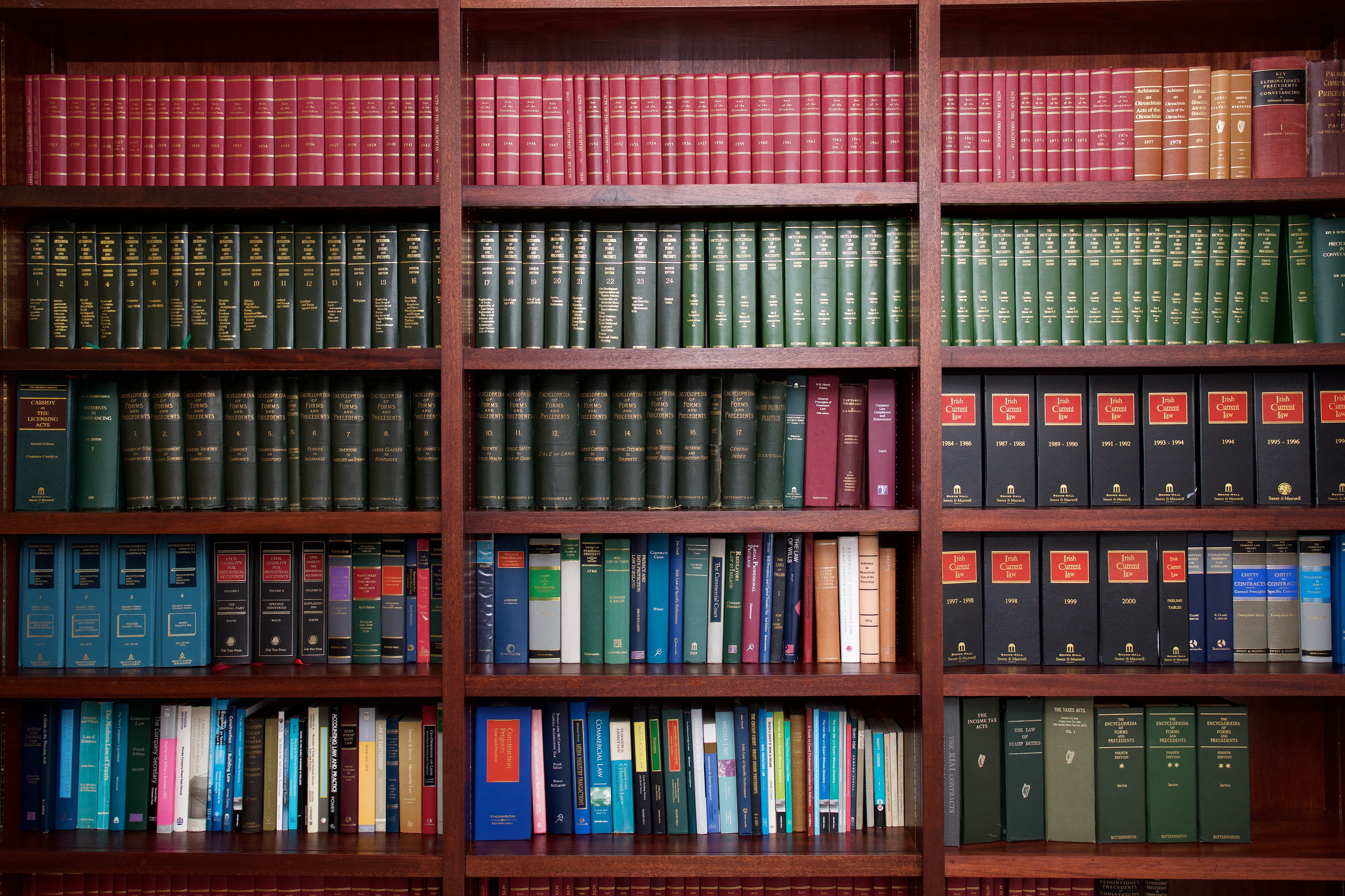 Books sit neatly on wooden shelves, organized by color and size, in a library setting.