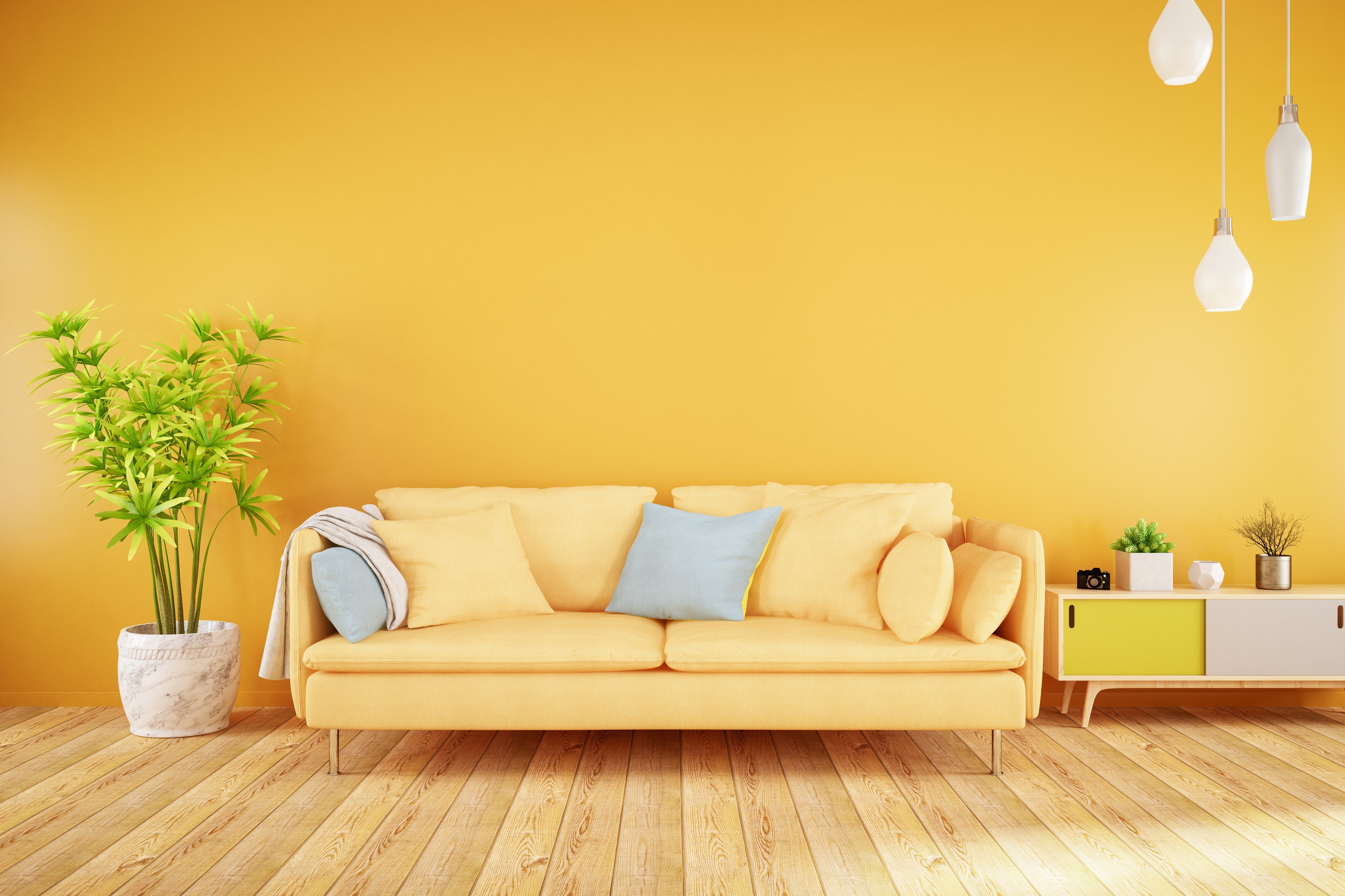 Yellow sofa sits in a vibrant room, surrounded by a potted plant, pendant lights, and a small sideboard on wooden flooring.