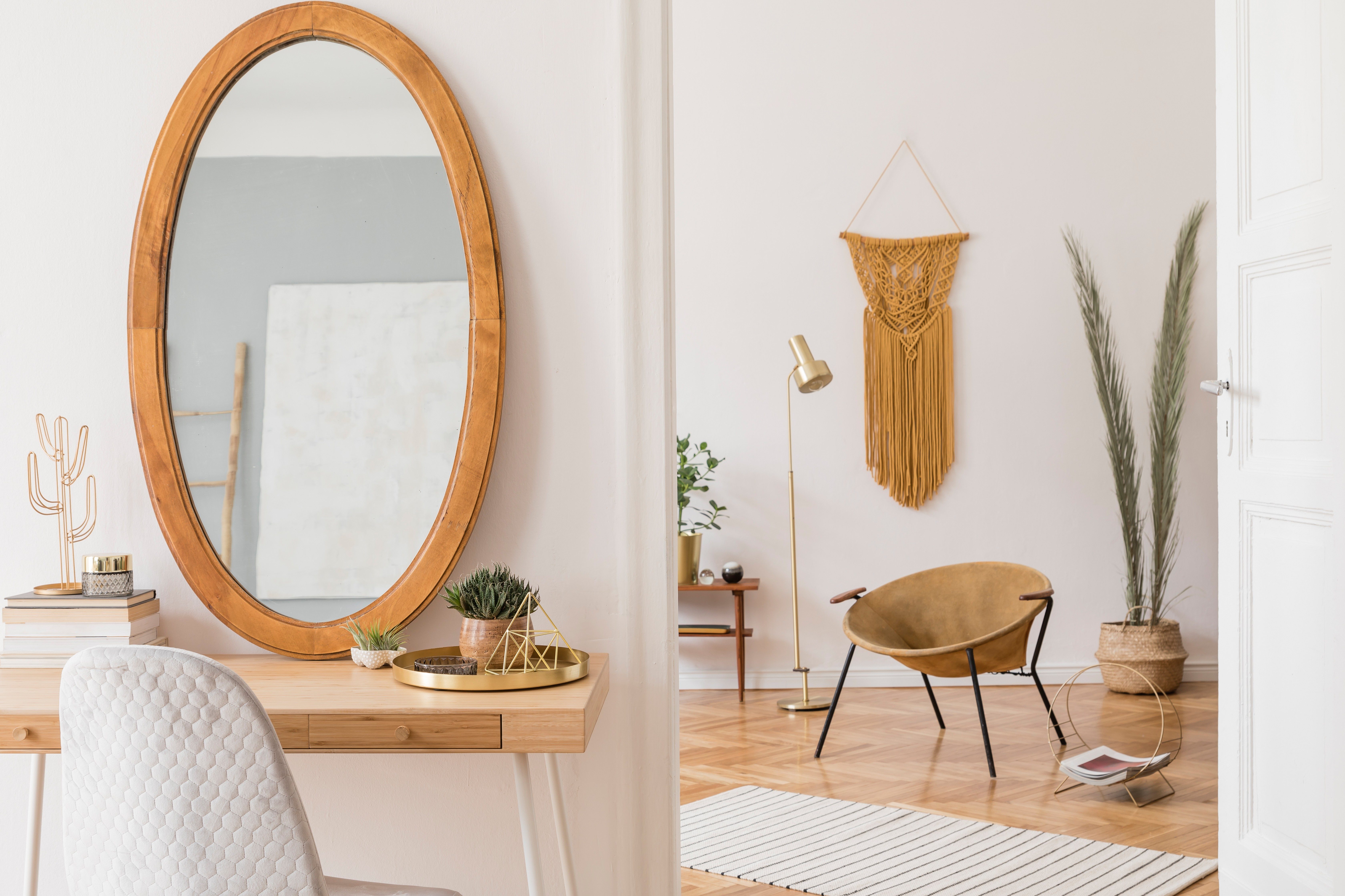 Oval mirror reflects room; placed on a wooden desk with books and decor, creating a cozy, stylish interior with a chair and plants.