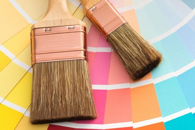 Brushes resting on a vibrant color swatch palette showing a spectrum of colors from yellow to blue, suggesting painting or design planning.