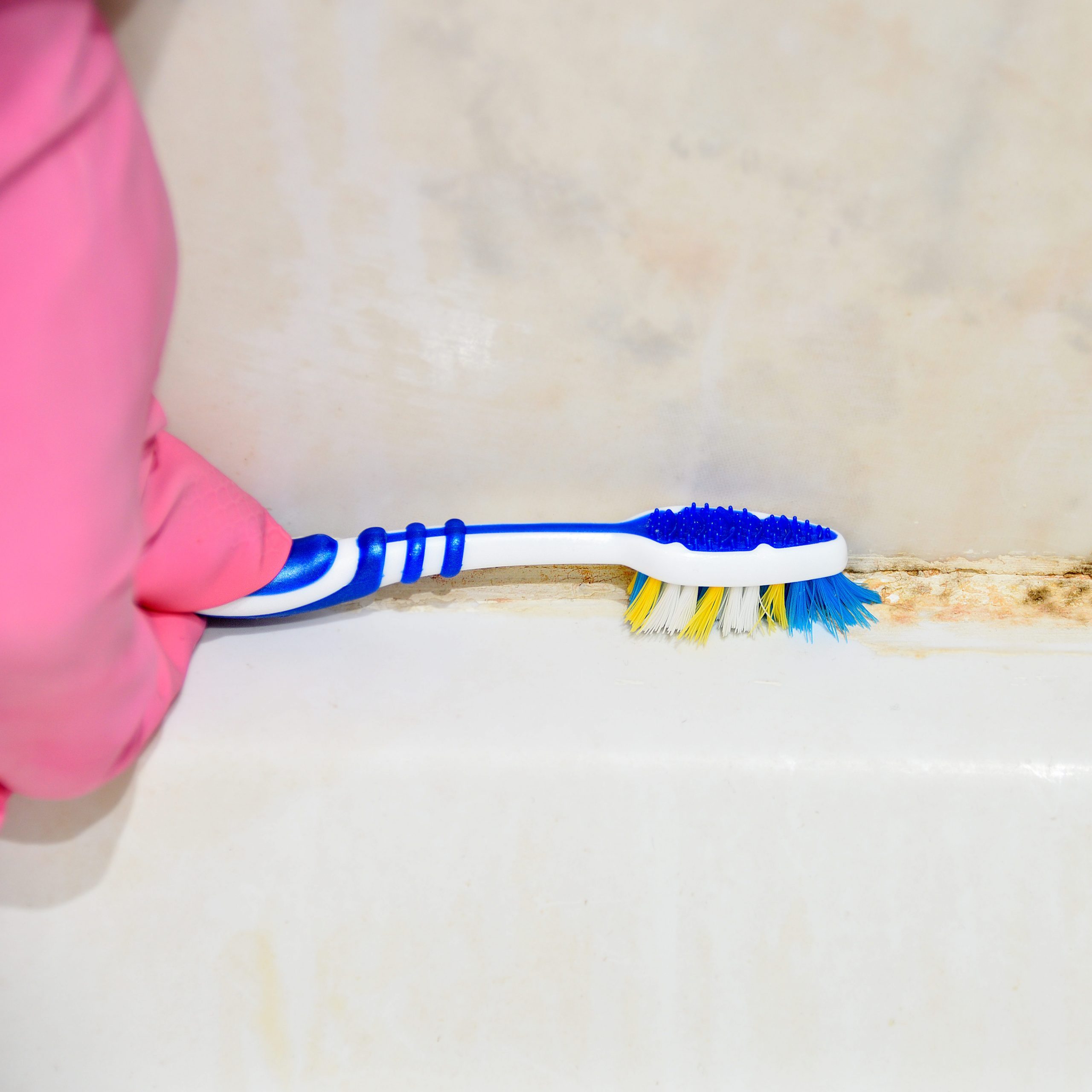 Cleaning moldy tile with a toothbrush at bathroom