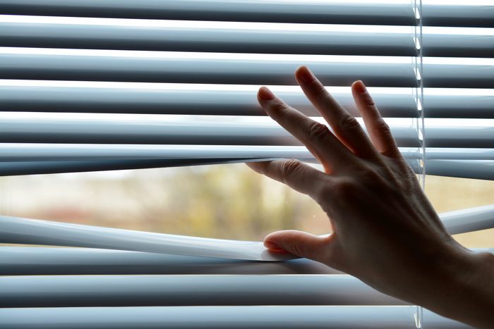 Female hand separating slats of venetian blinds with a finger to see through
