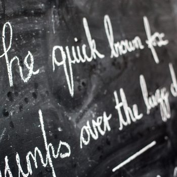 Chalk text reads "The quick brown fox jumps over the lazy dog" on a blackboard in a classroom setting.