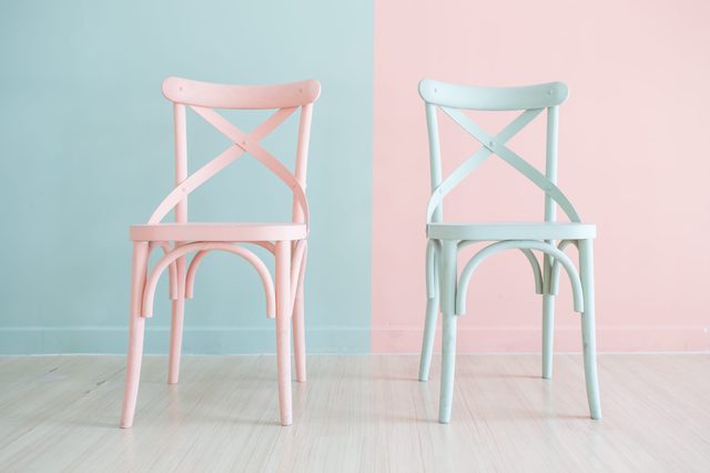 Two pastel chairs stand on a light wooden floor against a two-toned mint and peach wall.