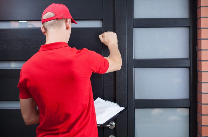 Back view of a delivery man knocking on the client's door