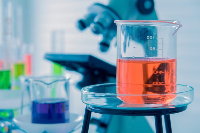 light red color liquid medicine in the glass beaker on the chemical tray with blurred liquid in beakers, test tubes, microscope in the Laboratory. Chemistry and science research concept.