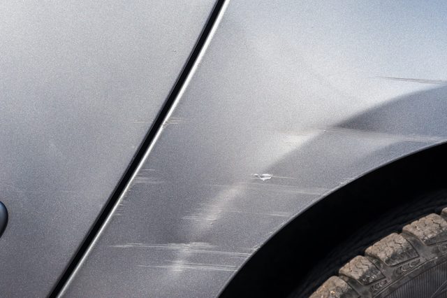 Car door has visible scratches and scuffs, shown against a background of metallic paint close to the wheel area.