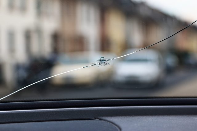 Cracked windshield, damaged, seen from inside a car with a street view background.