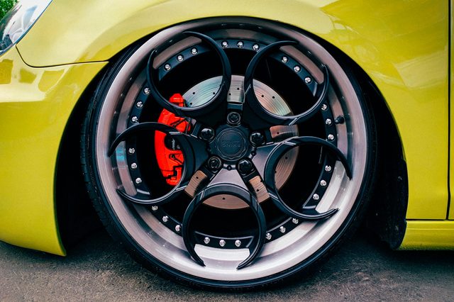 Wheel features intricate black design and red brake caliper, surrounded by a yellow car body, parked on asphalt.