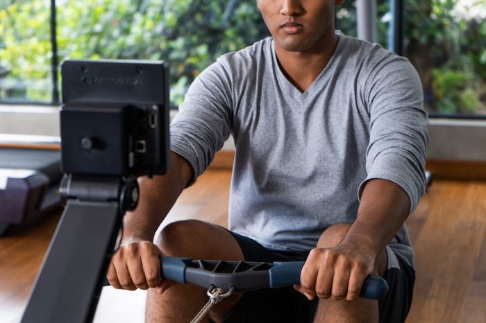 Athlete makes low cable pulley row seated in gym. Close back view