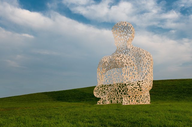 Sculpture composed of interconnected letters sits silently on a grassy hill under a partly cloudy sky.