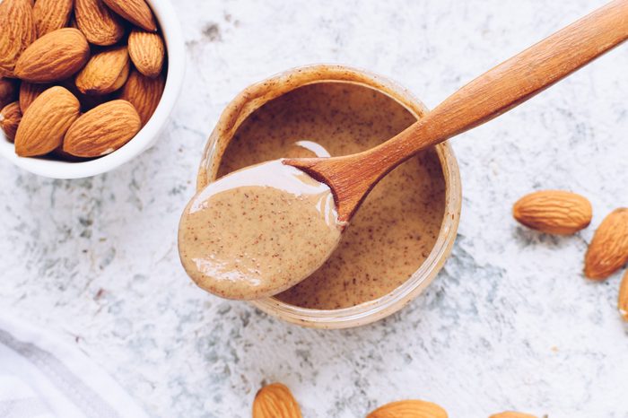Almond nut butter in glass jar. Homemade raw organic almond nuts paste on grey background. Healthy natural food concept. Top view.