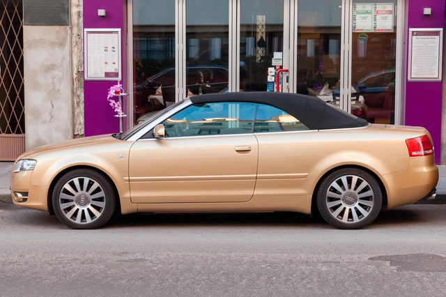 A gold convertible car is parked on a street, outside a building with purple walls and a menu displayed.