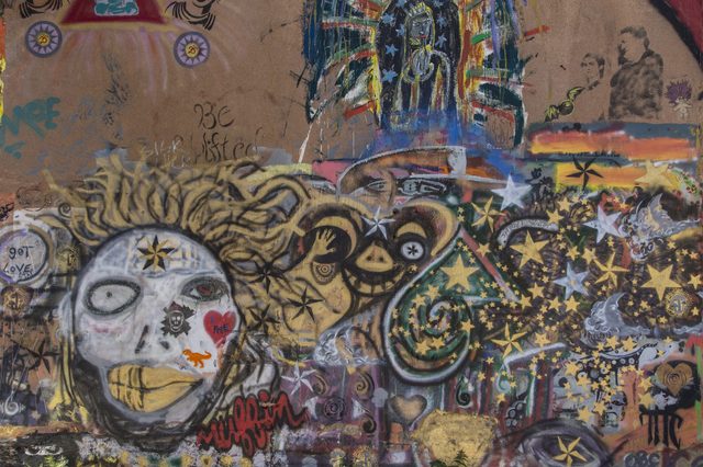 Graffiti mural depicting abstract faces, stars, and vibrant colors on a textured wall, creating a chaotic blend of patterns and symbols.