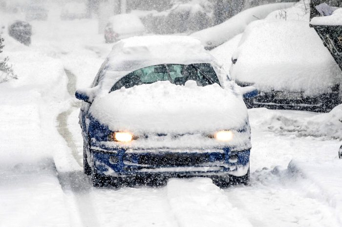 A snow covered car drives in winter storm