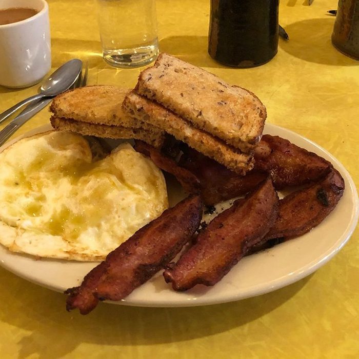 Plate with eggs, bacon, and stacked toast on a yellow table, surrounded by coffee, glass of water, and utensils.