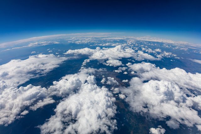 Clouds float beneath a deep blue sky, overlooking a distant landscape that stretches toward the horizon.