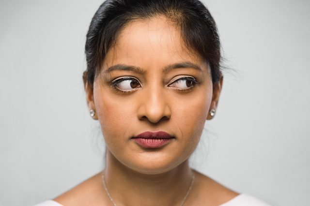 Woman looking sideways with a thoughtful expression, set against a plain gray background.