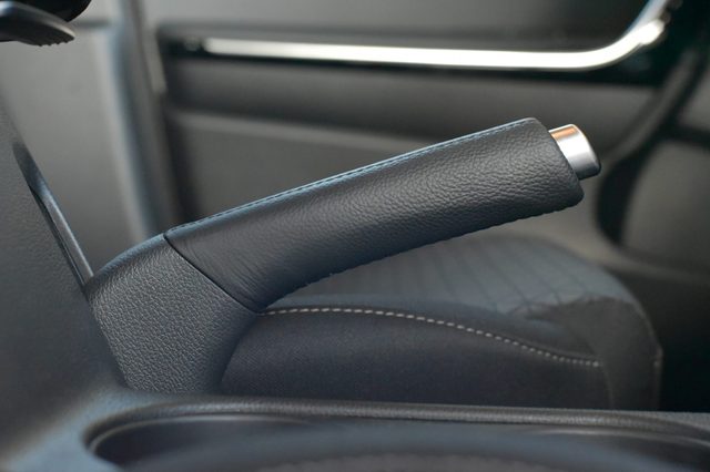 Handbrake lever resting in a car interior; black leather upholstery surrounds with silver metal tips visible.