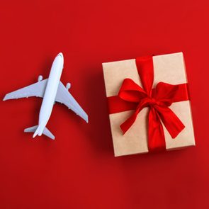 A small airplane model and wrapped gift box with a red ribbon sit on a bright red background.