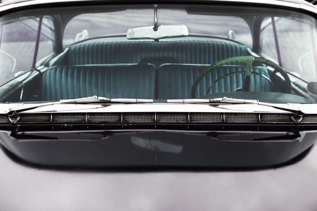 Classic car interior viewed through windshield, showing a green steering wheel and striped bench seat, set in a vintage vehicle ambiance.