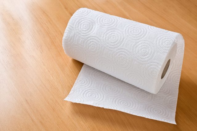 A roll of paper towel unrolls slightly on a wooden table.