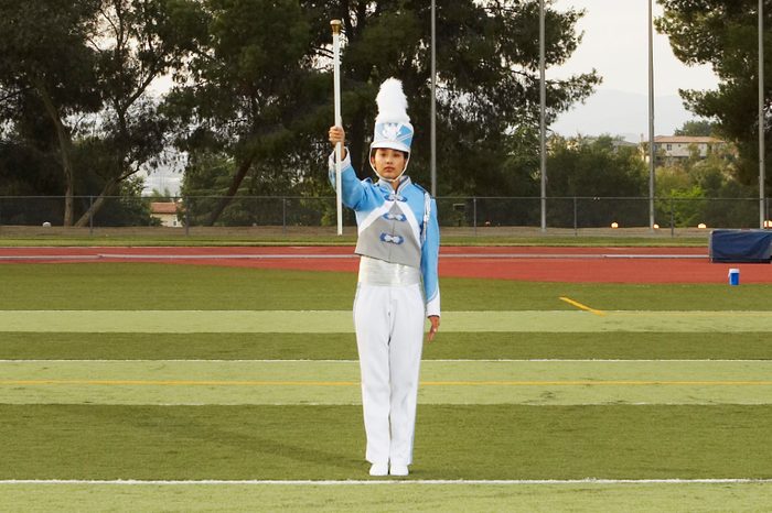 Female marching band member in full uniform on football field