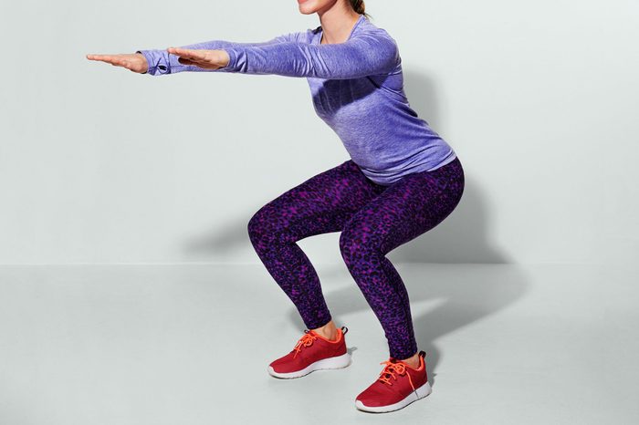 anonymous woman doing a squat. gray background.