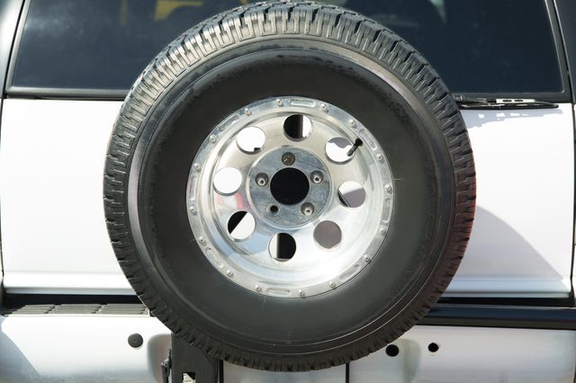 A spare tire is mounted on the rear of a white vehicle, set against a windowed backdrop.