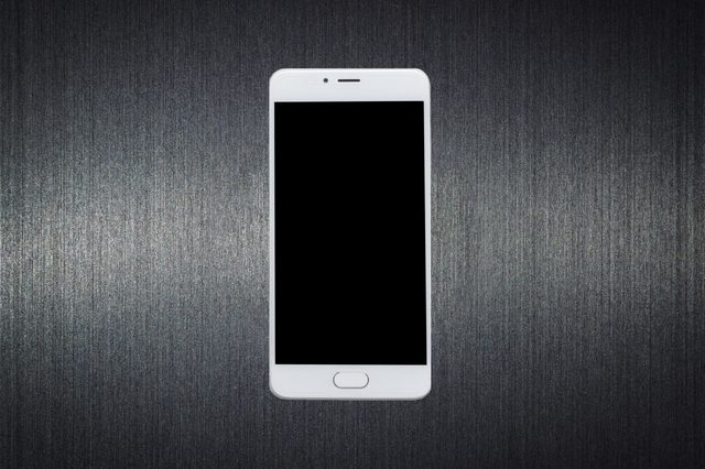 A white smartphone is displayed facing forward on a textured dark surface, screen turned off.