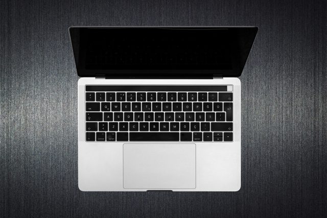 A laptop with an open screen displays on a textured dark surface, showing a QWERTY keyboard with additional characters.