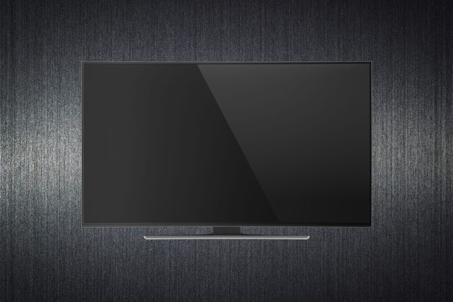 A flat-screen TV mounted on a textured, dark wall; it is turned off, reflecting light from the surrounding environment.