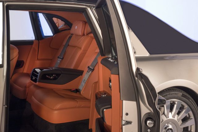 A luxurious car interior with tan leather seats, open rear doors, and visible wheel in a well-lit showroom setting.
