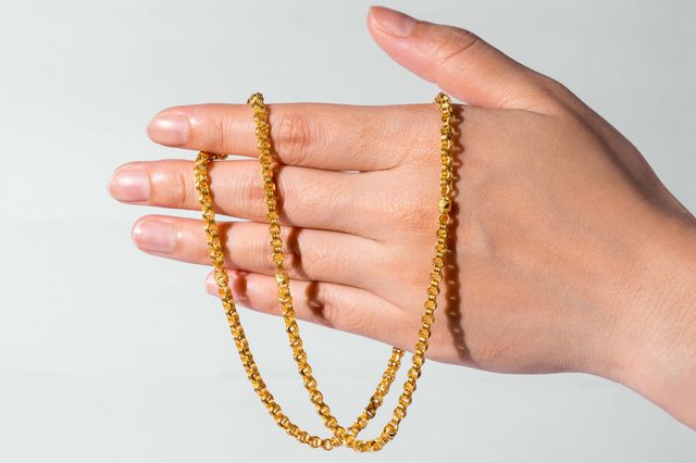 A hand holds a gold chain, draped across open fingers, set against a plain, light background.
