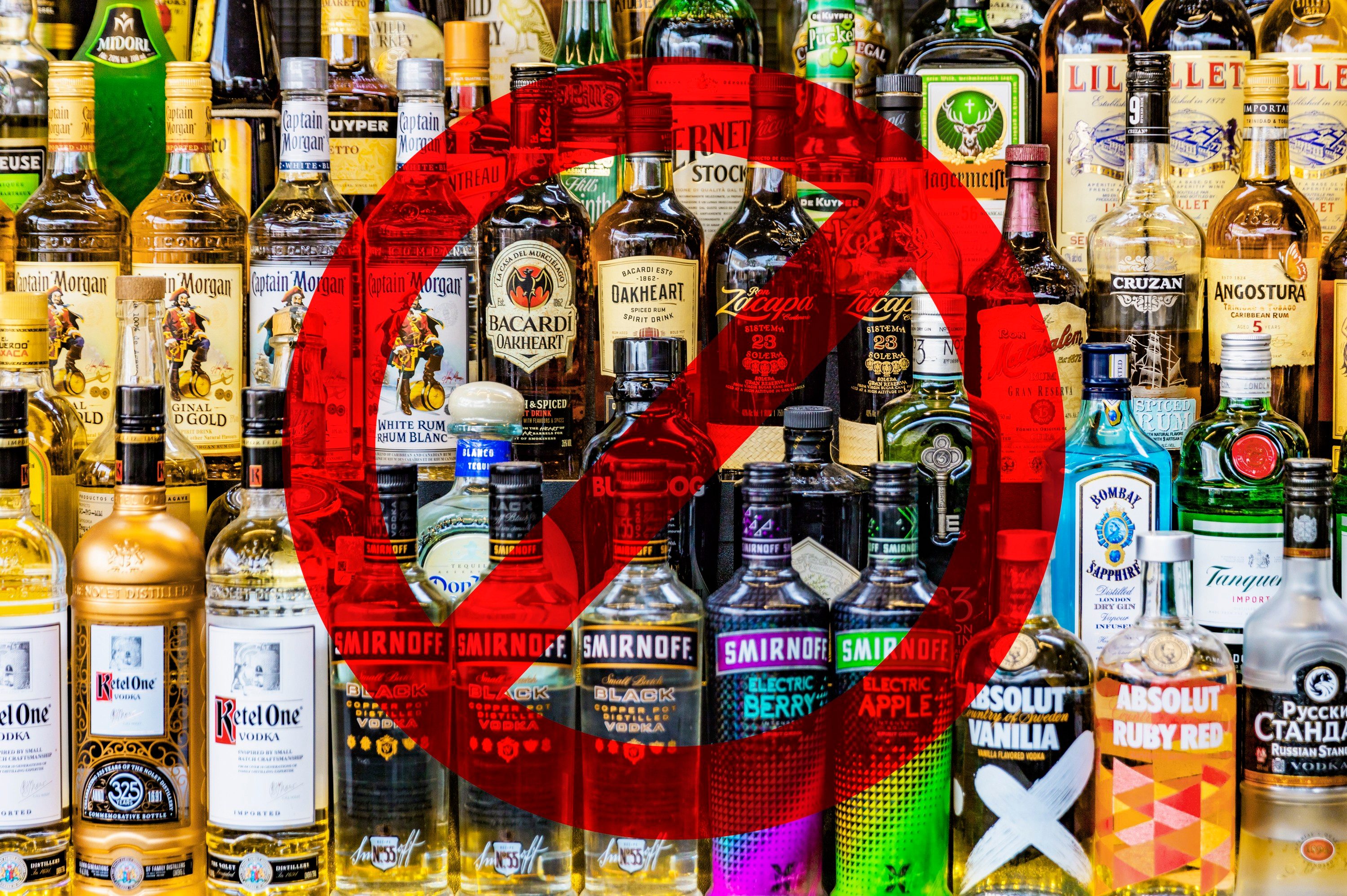 Bottles of various liquors stand with a red prohibition symbol overlaid, indicating a restriction. The background consists of diverse liquor brands.