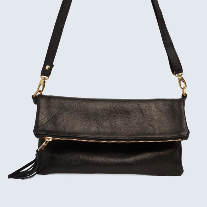 A black leather handbag hangs against a plain background, featuring a fold-over design, a gold zipper, and a tassel.