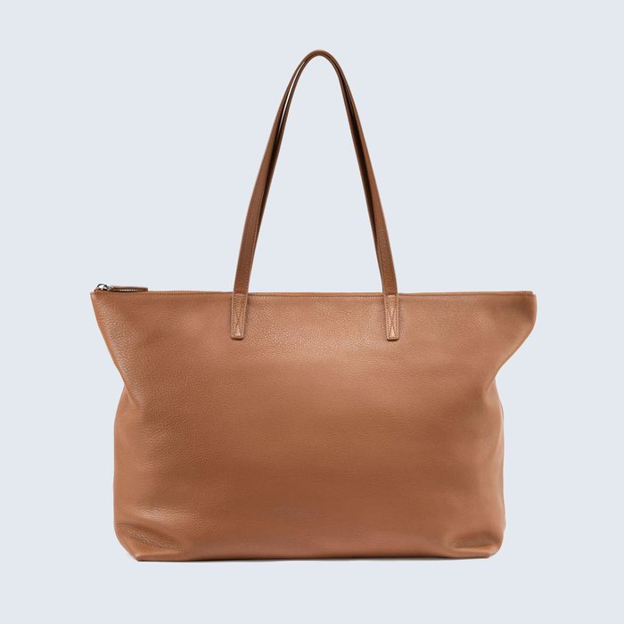 Brown leather tote bag sits against a plain, light background, featuring two handles and a zipper closure on top.